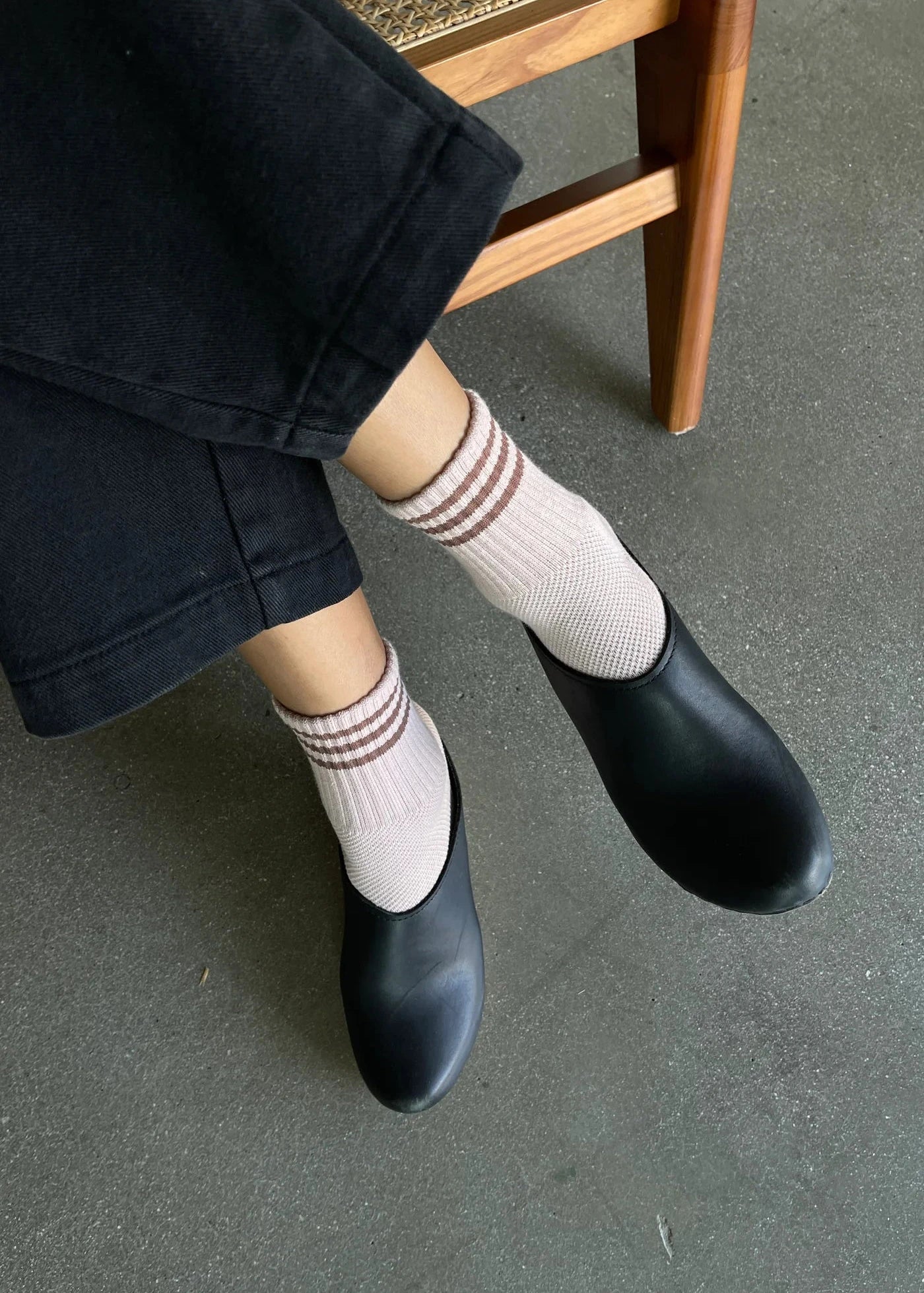 Person wearing black pants, pink socks with brown stripes and black shoes on concrete floor