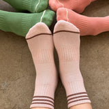 Person wearing pink socks, by other people's feet wearing green socks, peach socks and purple socks.