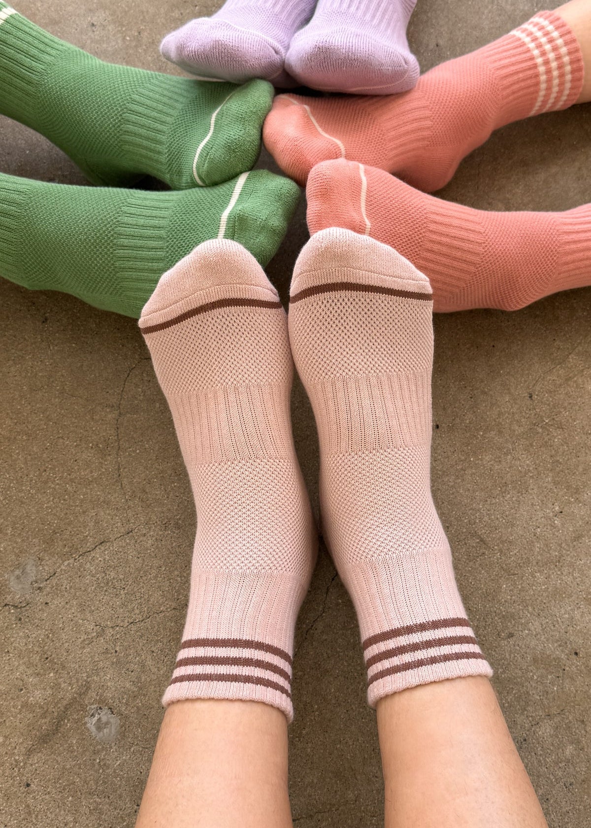 Person wearing pink socks, by other people's feet wearing green socks, peach socks and purple socks.