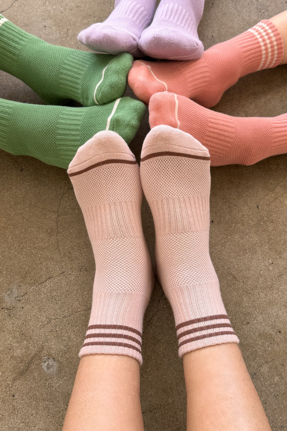 Person wearing pink socks, by other people's feet wearing green socks, peach socks and purple socks.