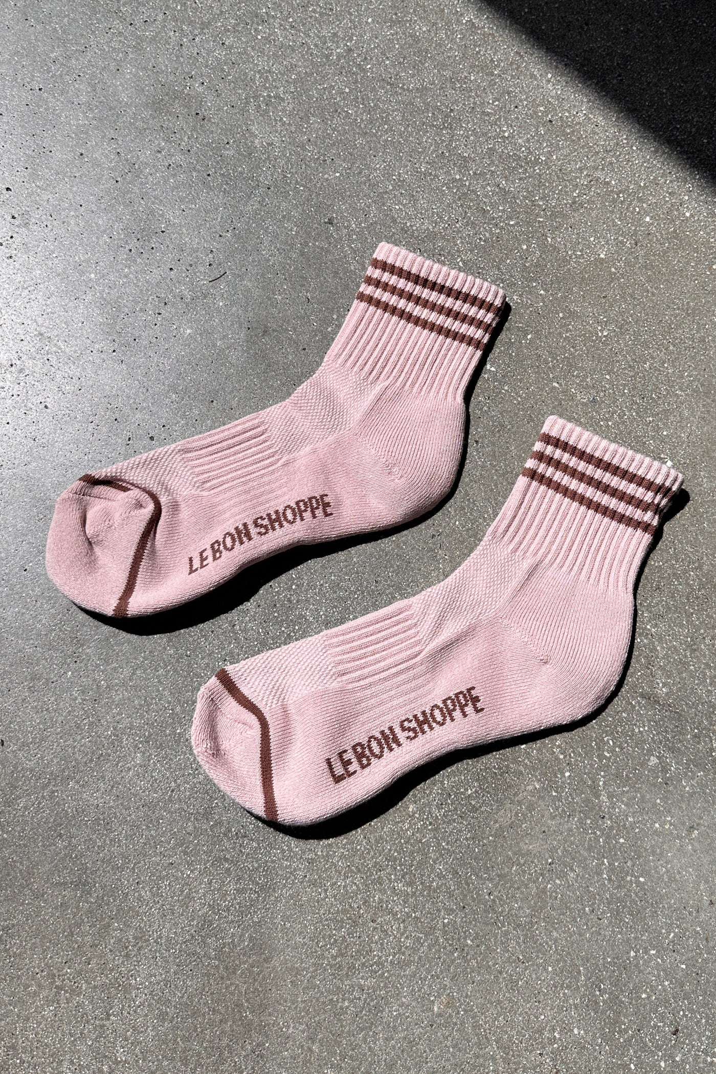 Pink socks with brown stripes with Le Bon Shop branding on concrete floor