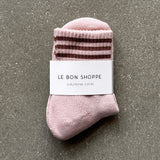 Pink socks with brown stripes in white Le Bon Shoppe packaging on concrete floor