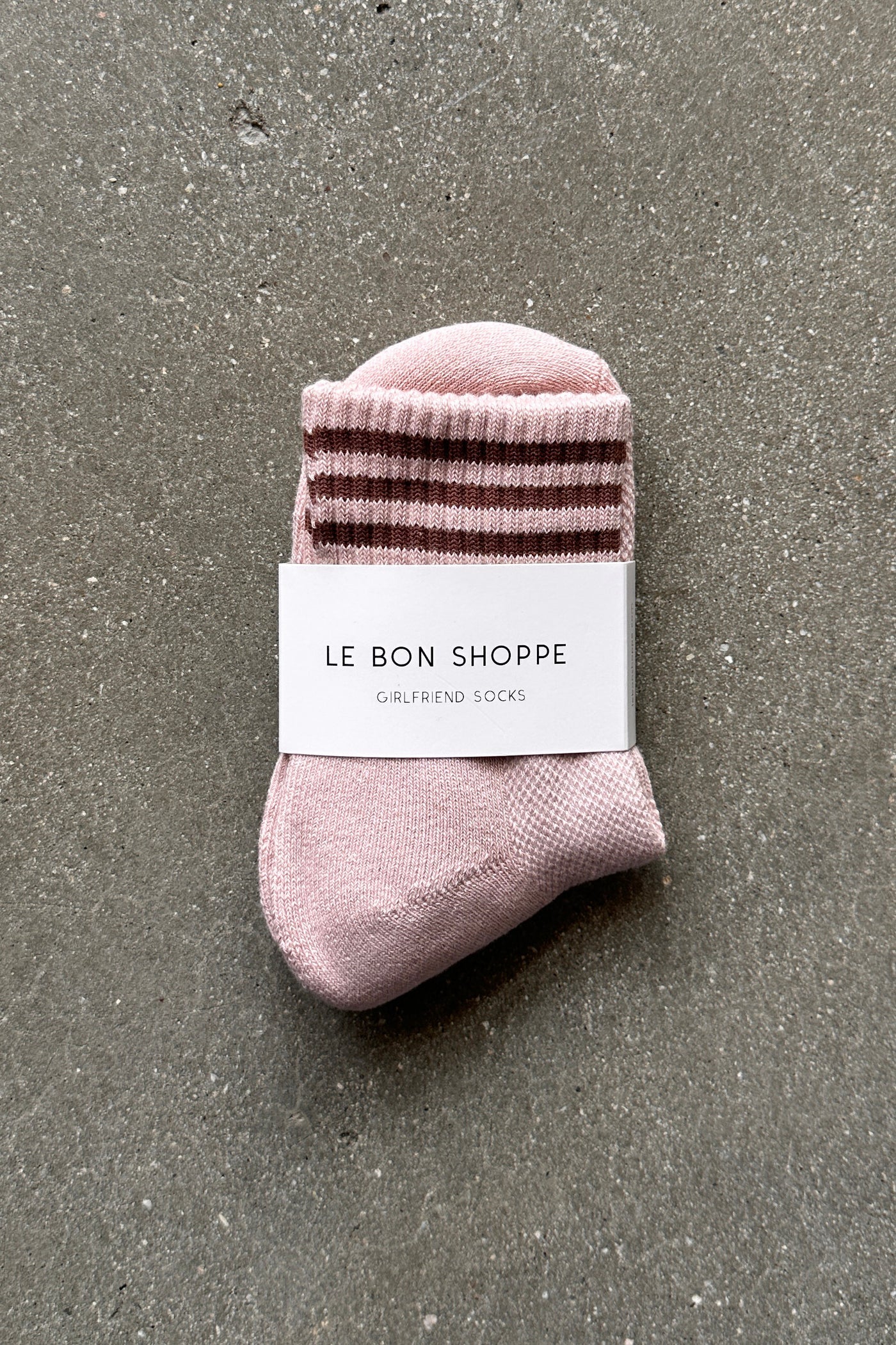 Pink socks with brown stripes in white Le Bon Shoppe packaging on concrete floor