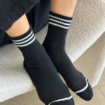 A pair of black ankle crew socks with a triple contrast stripe at the opening, worn on someone's feet.