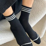 A pair of black ankle crew socks with a triple contrast stripe at the opening, worn on someone's feet.