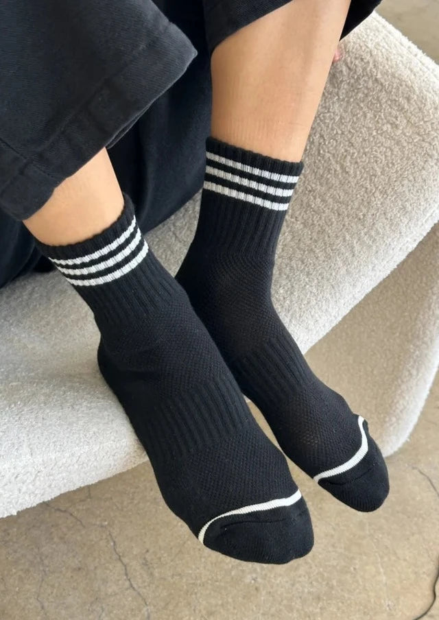 A pair of black ankle crew socks with a triple contrast stripe at the opening, worn on someone's feet.