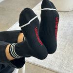 Person wearing black socks with white stripes and red Le Bon Shoppe branding 