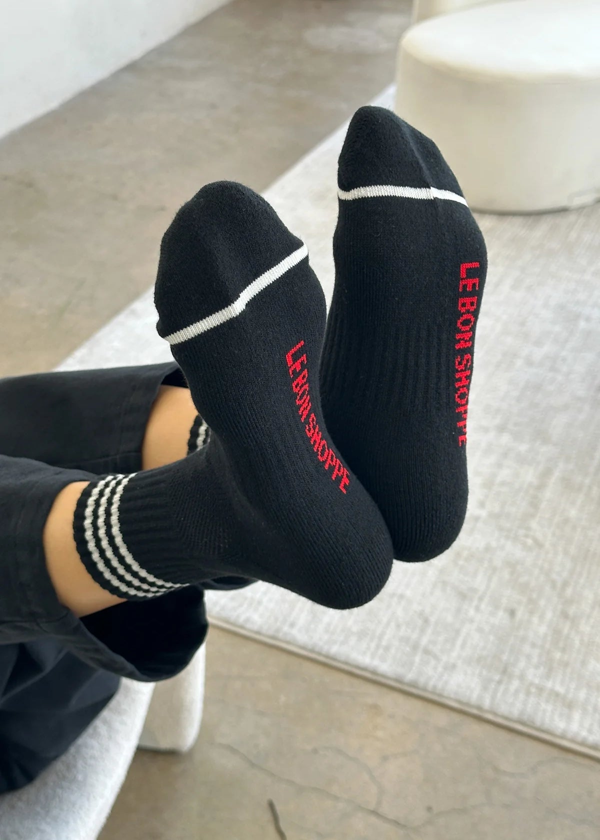 Person wearing black socks with white stripes and red Le Bon Shoppe branding 