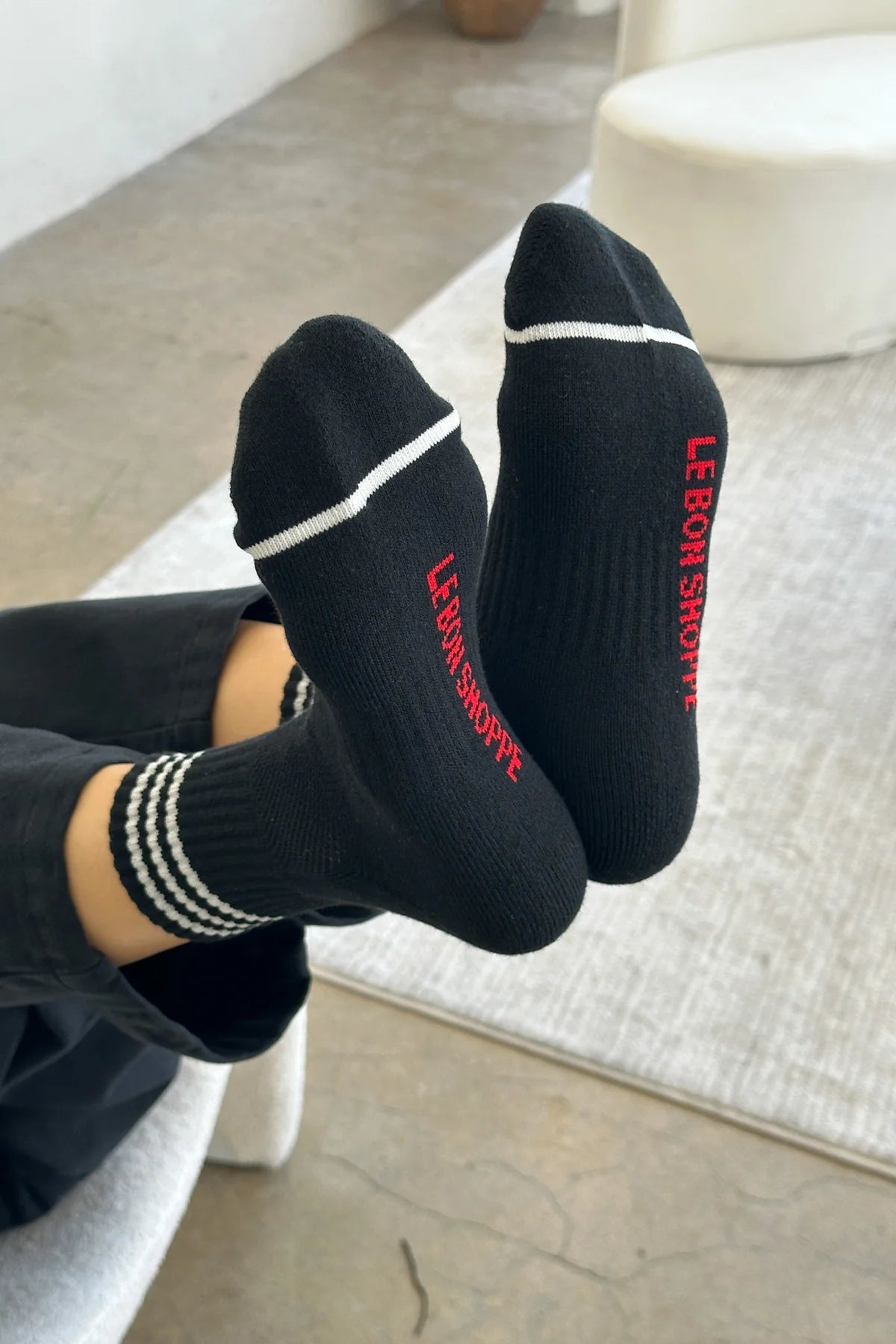 Person wearing black socks with white stripes and red Le Bon Shoppe branding 