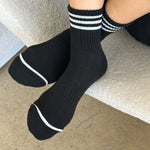 Person wearing black socks with white stripes on carpet floor.