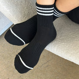 Person wearing black socks with white stripes on carpet floor.