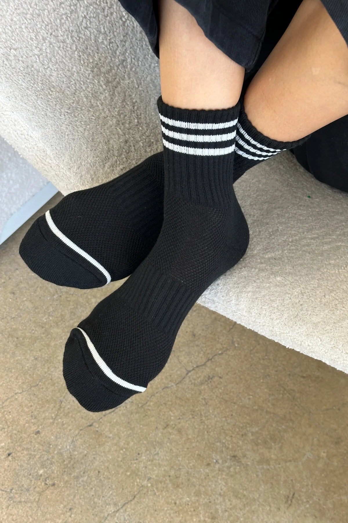 Person wearing black socks with white stripes on carpet floor.