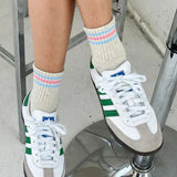 Person wearing white sneakers with green accents and colorful striped socks on a metal stool.