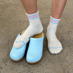 Light blue clogs worn with white socks on a concrete surface