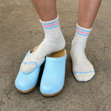 Light blue clogs worn with white socks on a concrete surface