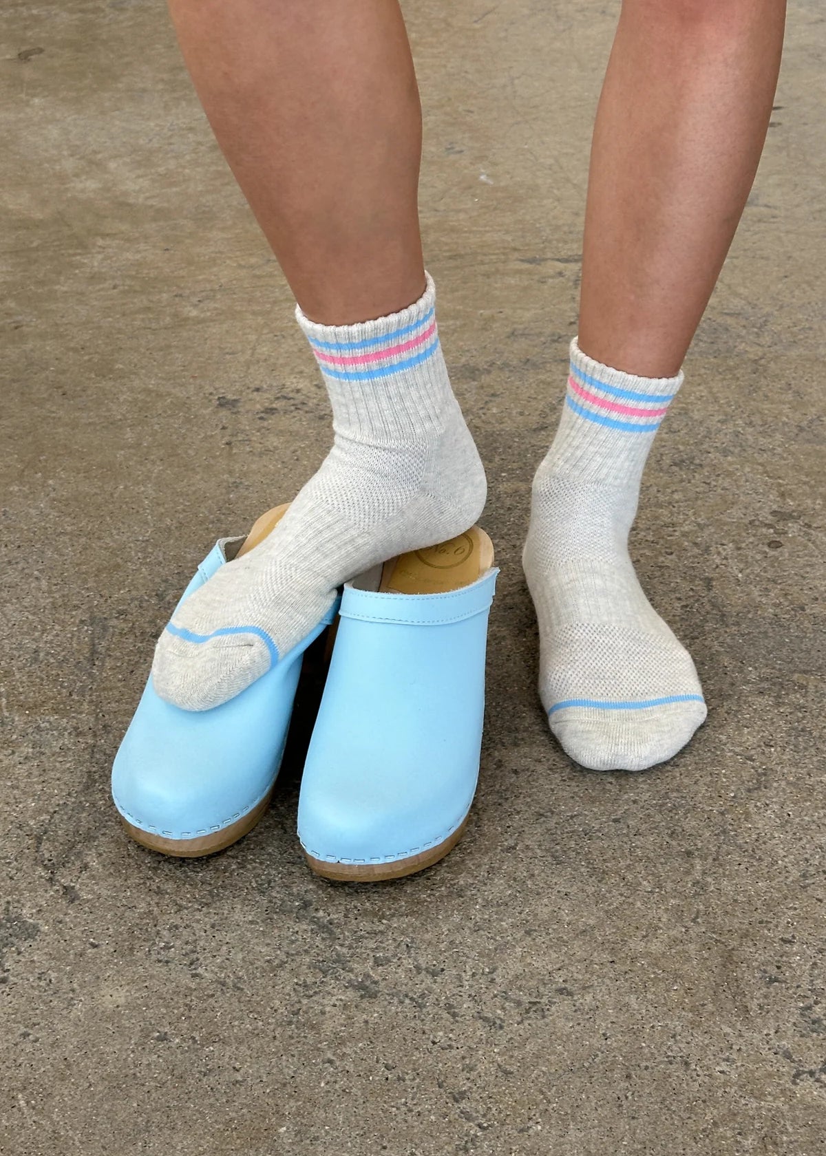 Light blue clogs worn with white socks on a concrete surface