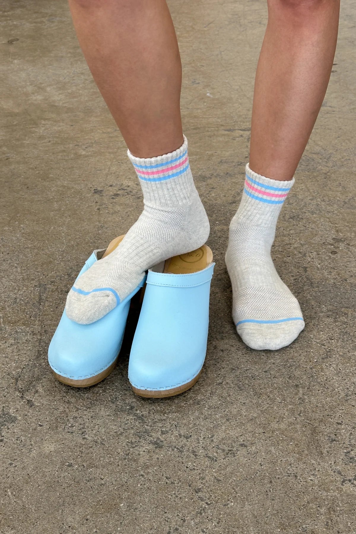 Light blue clogs worn with white socks on a concrete surface