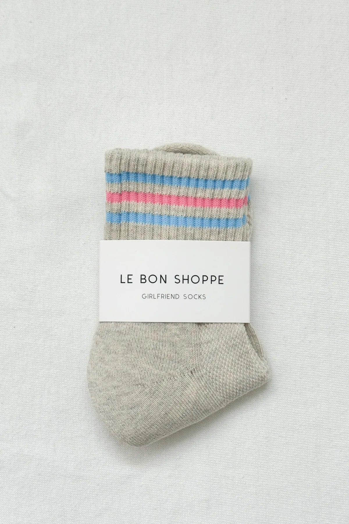 Gray sock with colorful stripes and 'Le Bon Shoppe' label on a light gray background