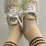 A person's fee raised in the air wearing yellow socks with brown stripes in floral sneakers with light grey background