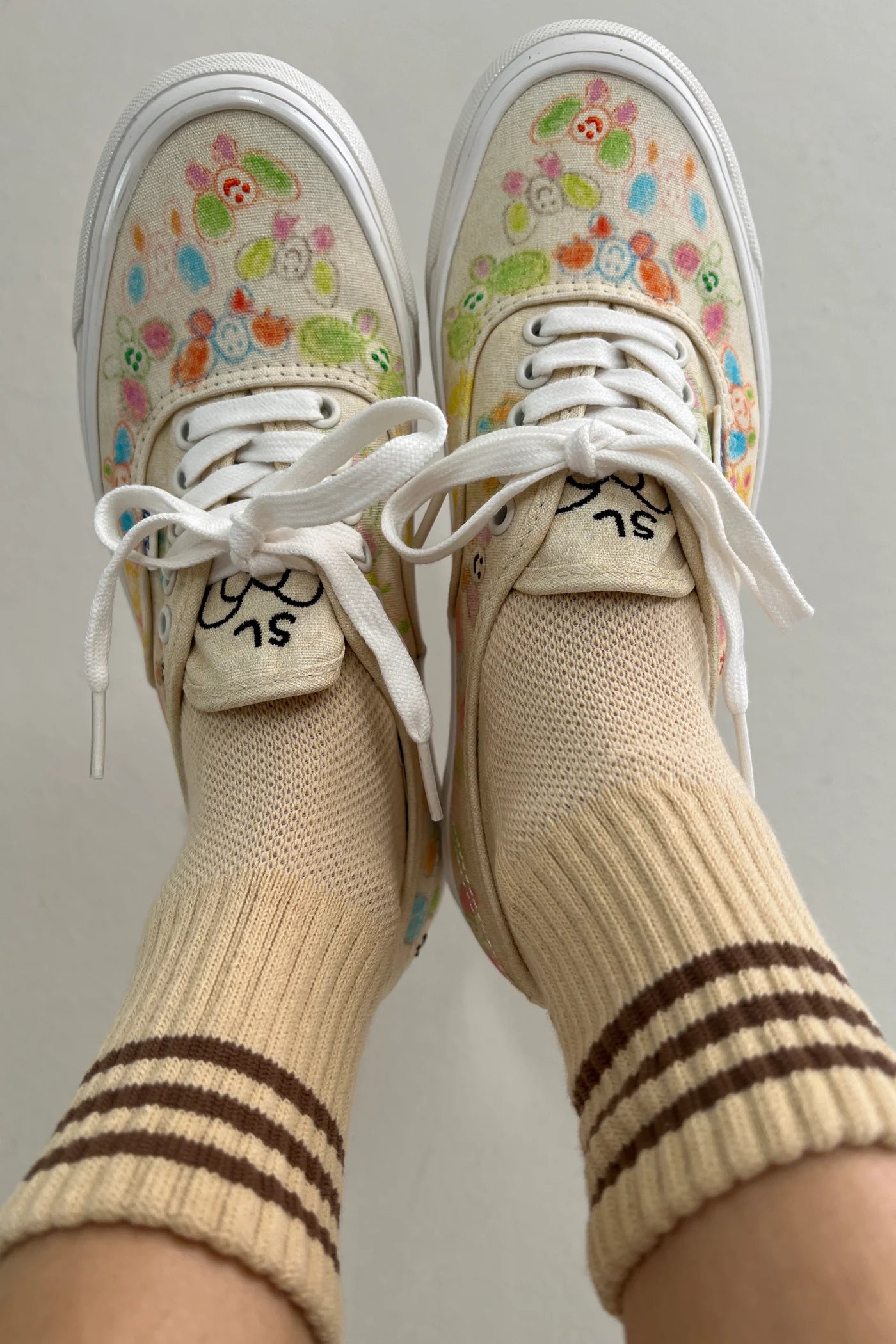 A person's fee raised in the air wearing yellow socks with brown stripes in floral sneakers with light grey background