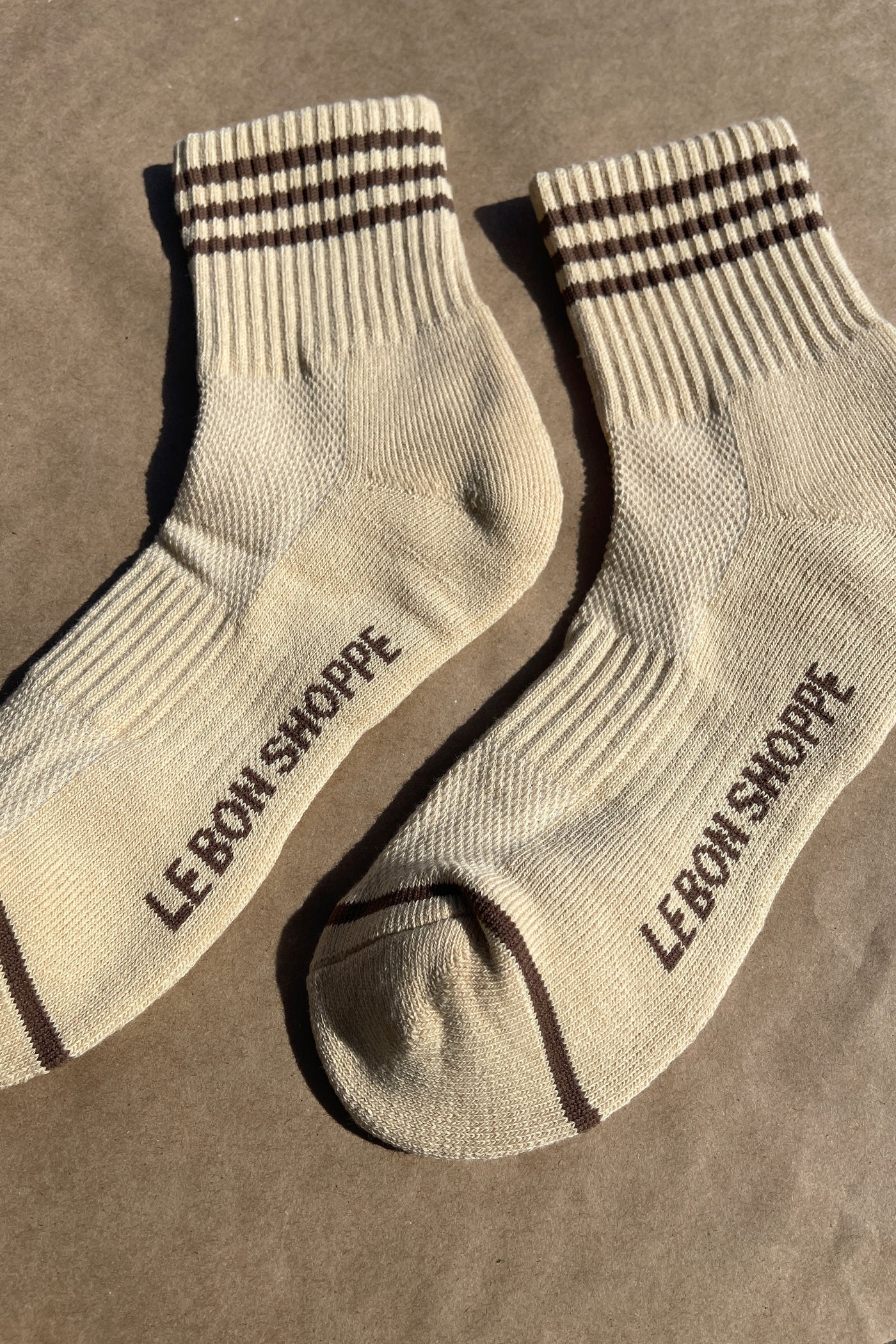Yellow socks with brown stripes and Le Bon Shoppe branding with kraft paper background