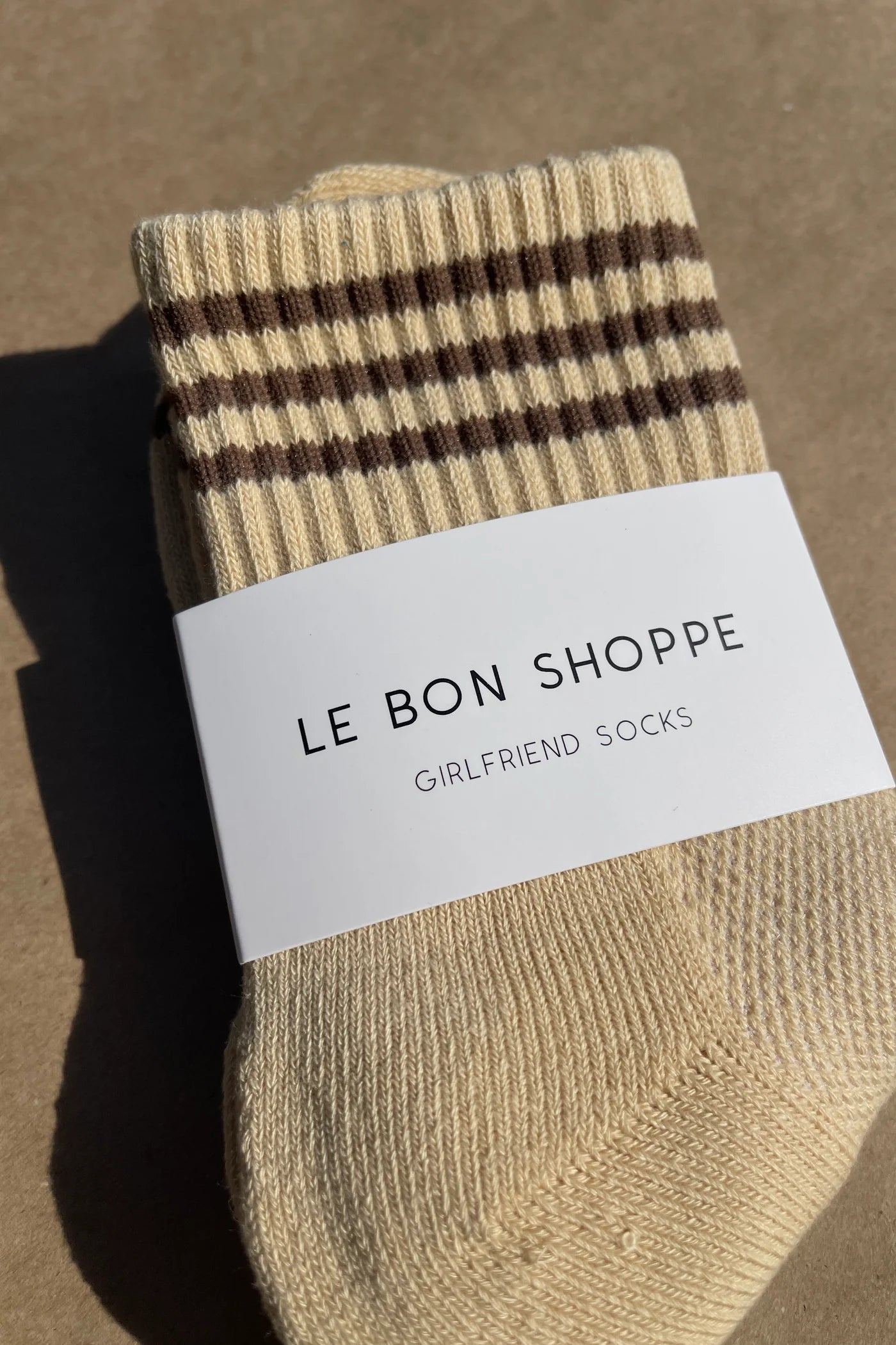 Yellow socks with brown stripes in white Le Bon Shoppe packaging with kraft paper background