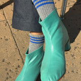 Person wearing black pants, grey socks with blue stripes and teal booties on the concrete floor.
