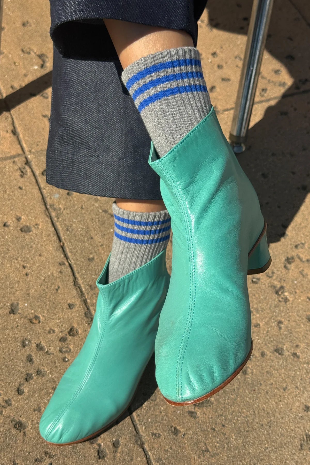 Person wearing black pants, grey socks with blue stripes and teal booties on the concrete floor.