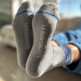 Person wearing grey socks with blue stripes and Le Bon Shoppe branding with windows in the background