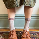 Person wearing brown shoes with fringes, plaid skirt, and checkered socks on a patterned rug.