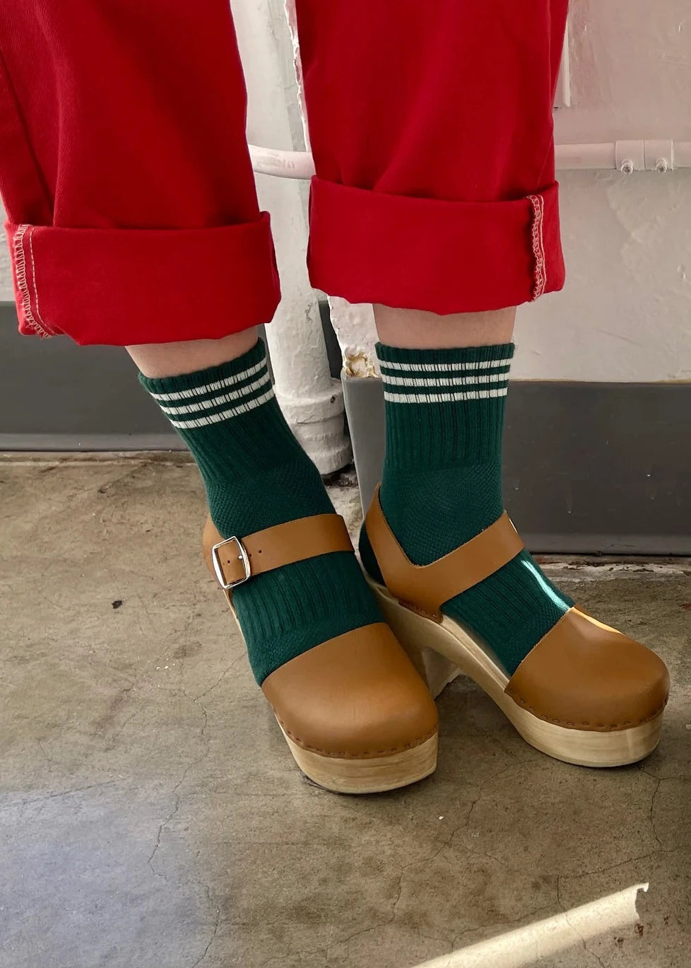 A pair of green ankle crew socks with a triple contrast stripe at the opening, worn with red pants and brown shoes.