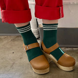 A pair of green ankle crew socks with a triple contrast stripe at the opening, worn with red pants and brown shoes.