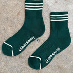 Green socks with white stripes and white Le Bon Shoppe branding on a concrete background