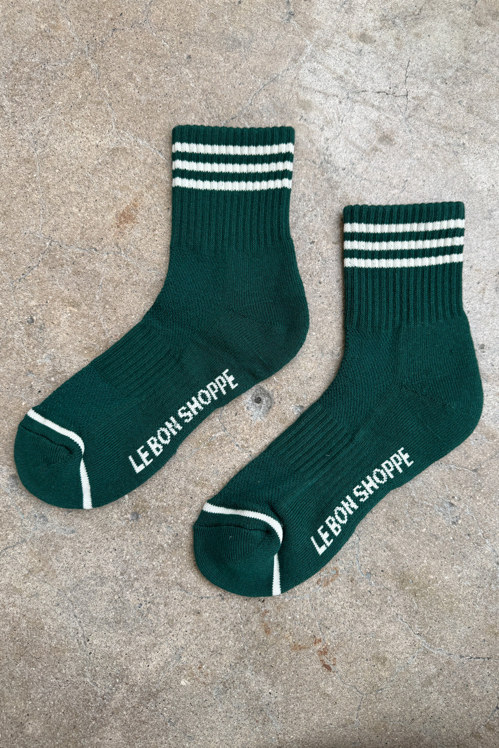 Green socks with white stripes and white Le Bon Shoppe branding on a concrete background