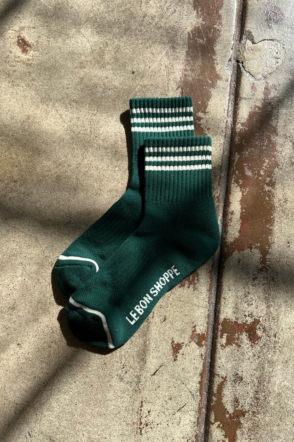 Green socks with white stripes laying in the sun on a concrete background