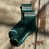 Green socks with white stripes laying in the sun on a concrete background