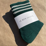 Green socks in white Le Bon Shoppe packaging on kraft paper background