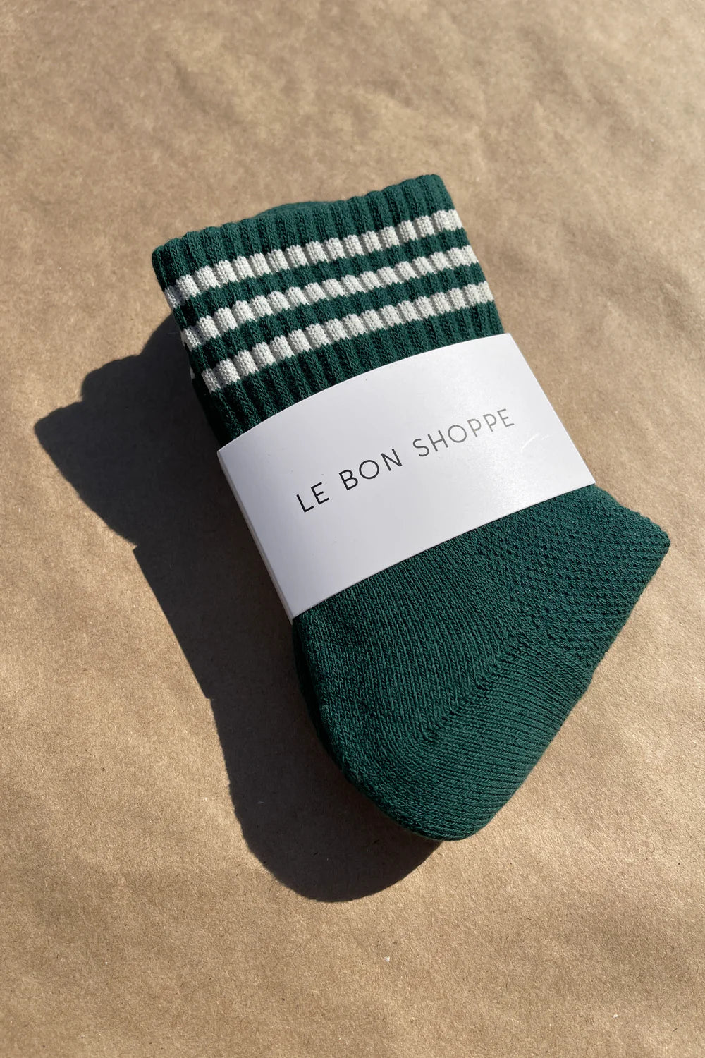 Green socks in white Le Bon Shoppe packaging on kraft paper background