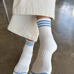person wearing white socks with blue stripes and cream colored pants on concrete floor