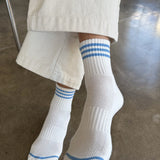 person wearing white socks with blue stripes and cream colored pants on concrete floor