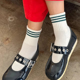 Person wearing black clogs with white socks and red pants on a concrete floor.