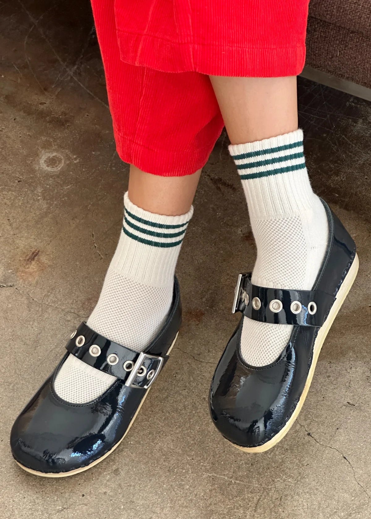 Person wearing black clogs with white socks and red pants on a concrete floor.