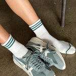 Person wearing green sneakers and white socks with green stripes on a concrete floor.