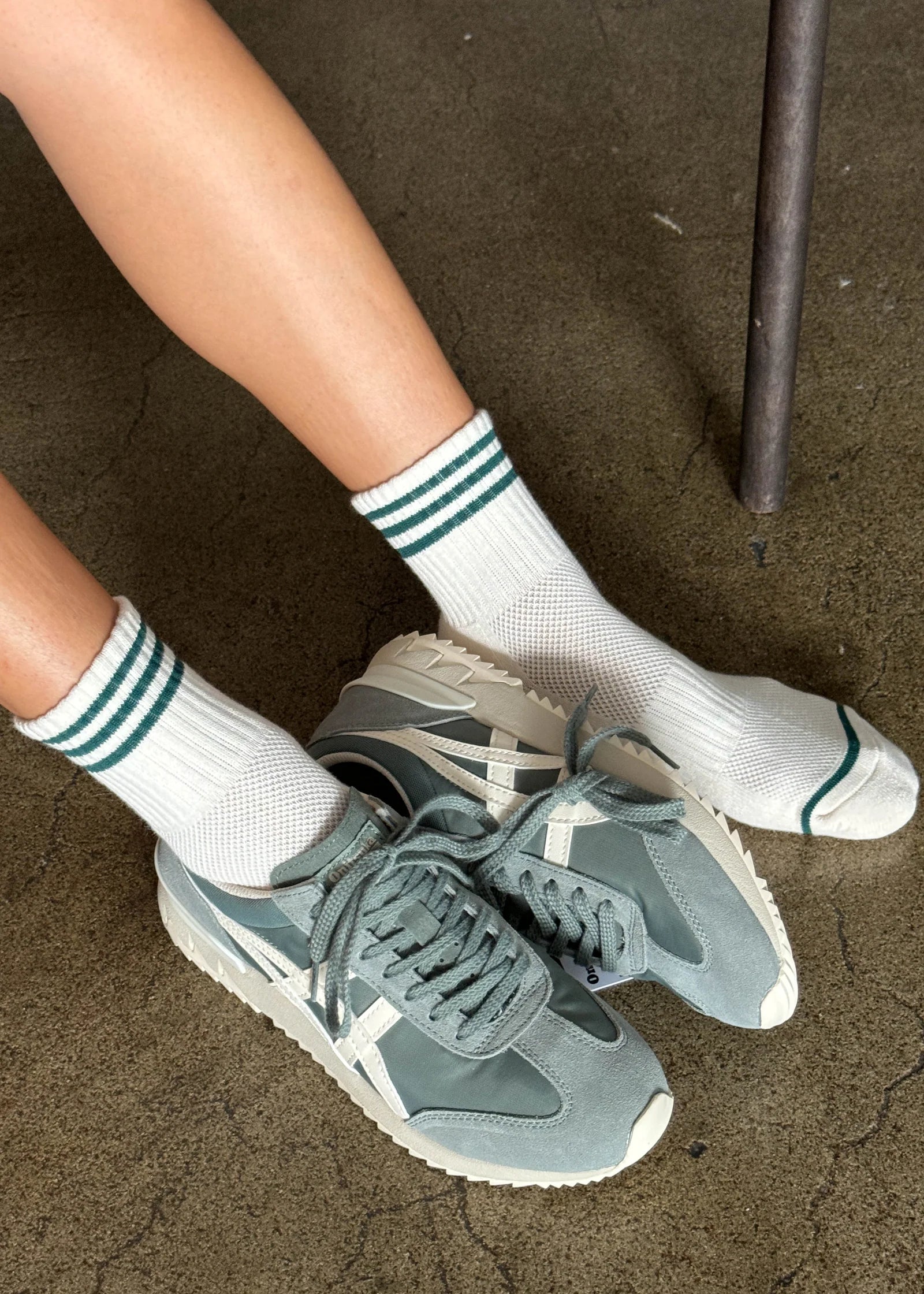 Person wearing green sneakers and white socks with green stripes on a concrete floor.