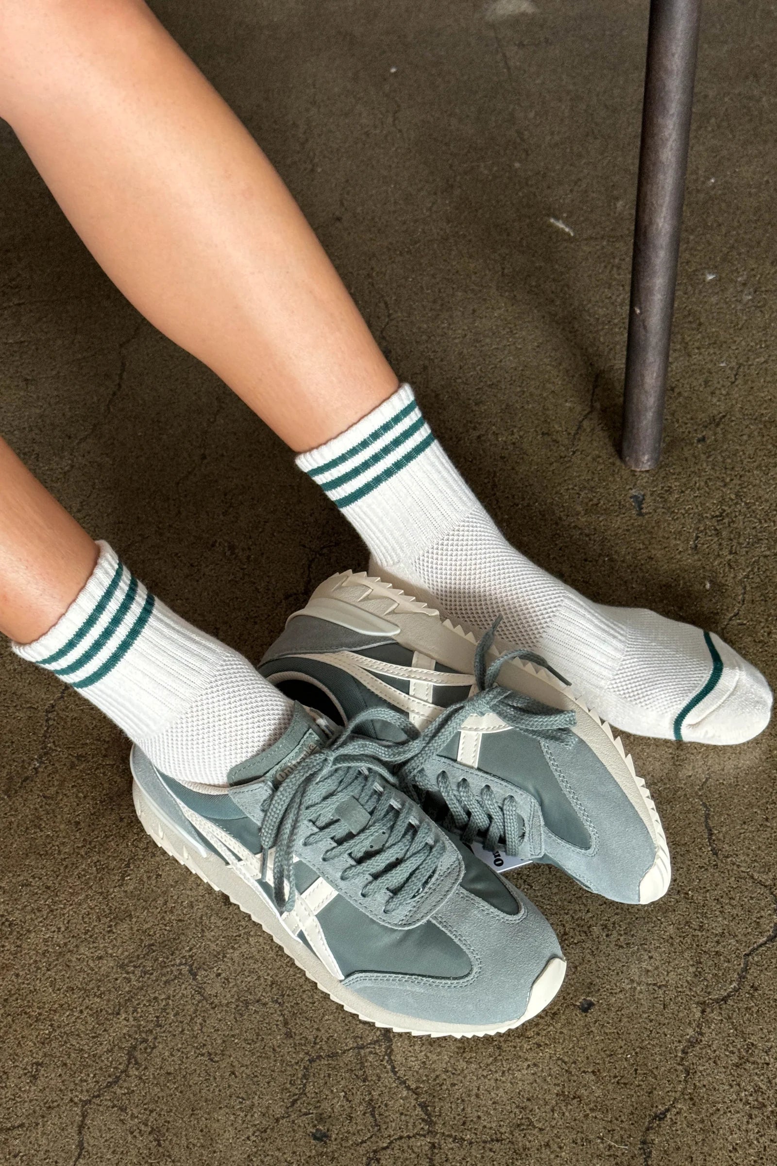 Person wearing green sneakers and white socks with green stripes on a concrete floor.