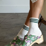 Person wearing green floral clogs with white socks on a gray floor.
