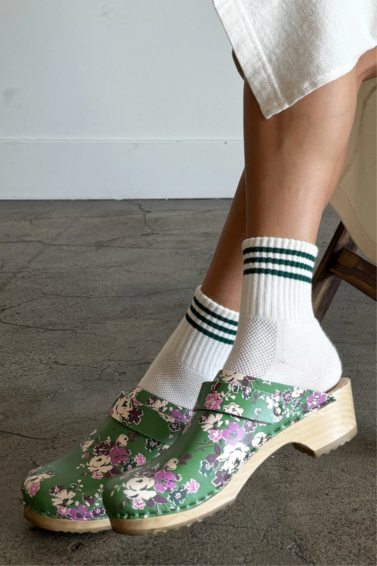 Person wearing green floral clogs with white socks on a gray floor.