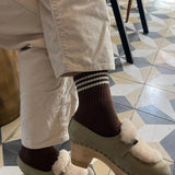 Person wearing cream colored pants, brown socks and taupe mules on tile checked floor