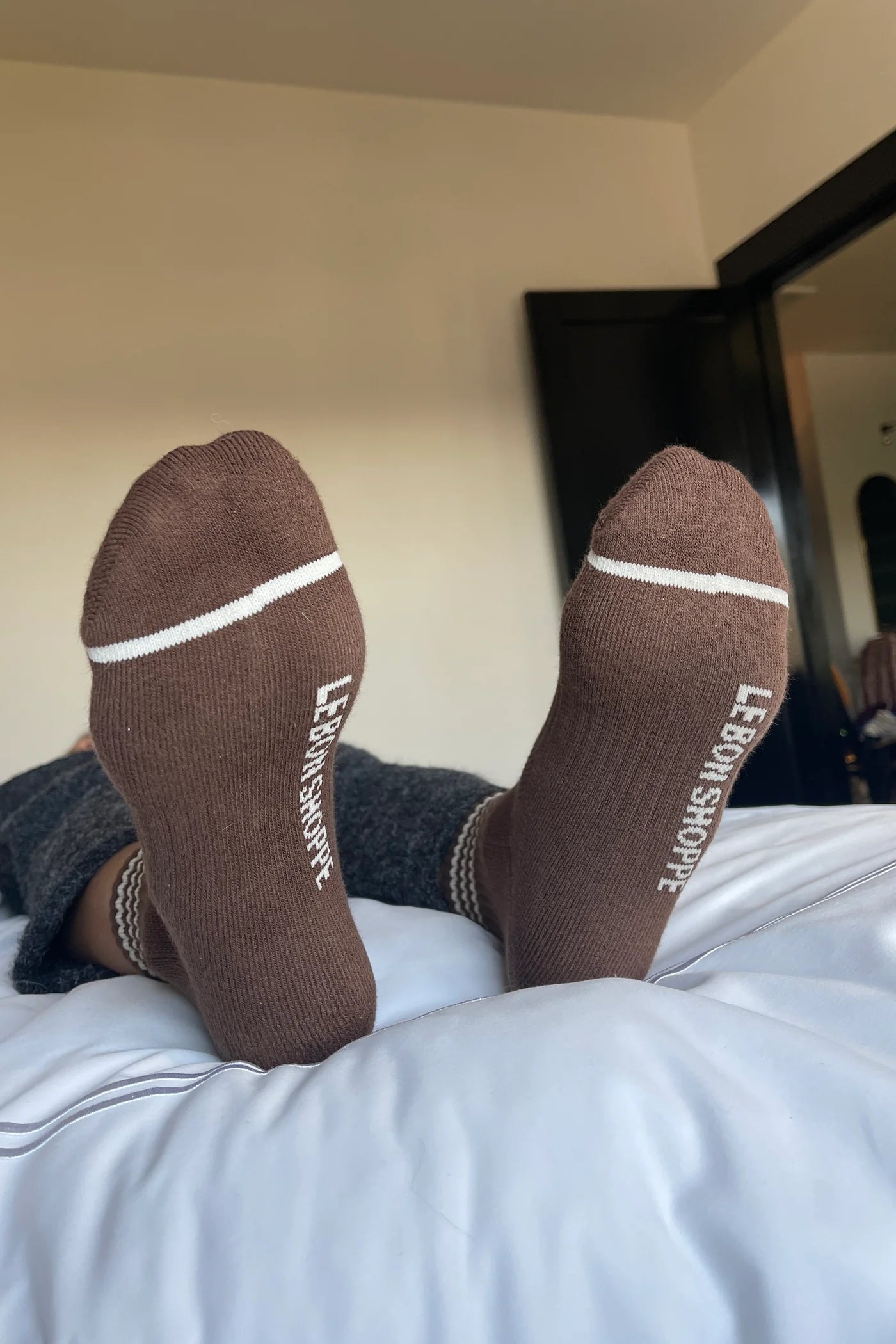 person wearing grey pants and brown socks with white stripes on a bed with white sheets