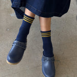 Person wearing navy clogs and socks with yellow stripes on a concrete floor.